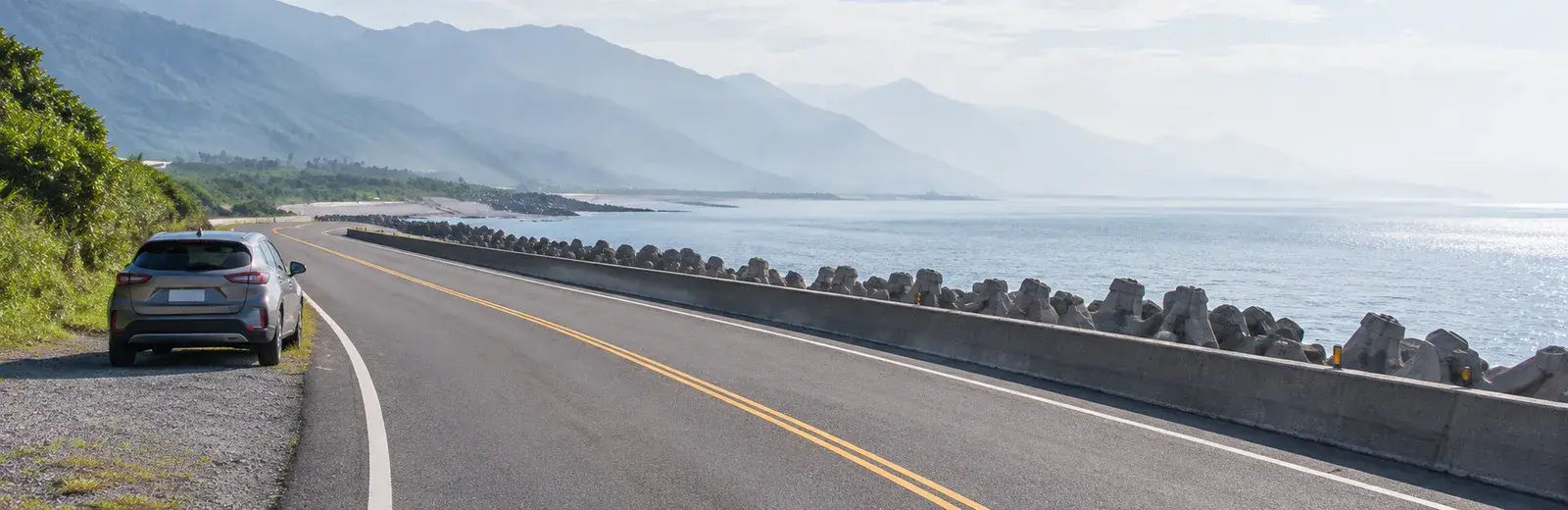 濱海公路旁的停靠點，車停在路肩，前方整段公路沿著消波塊海岸延伸